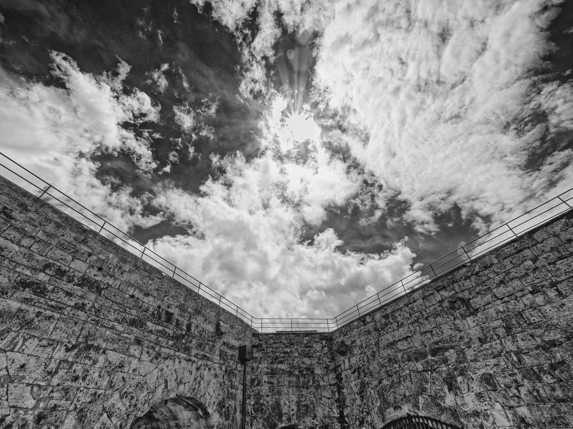 Von links und rechts zulaufende Burgmauer mit Himmel dahinter in schwarz-weiß.