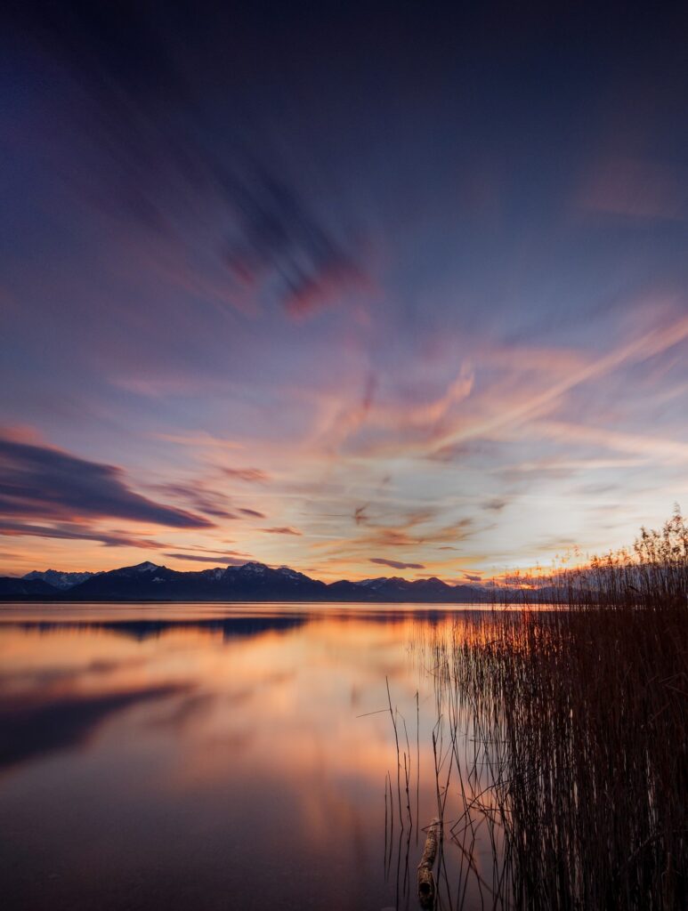 Rosa-oranger Schimmer in den Wolken, der sich auf dem See widerspiegelt. Langzeitbelichtung mit 50 Sekunden.