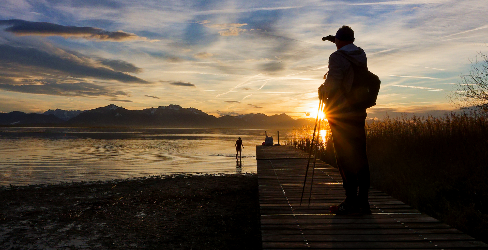 Mann auf Steg guckt in Sonnenuntergang