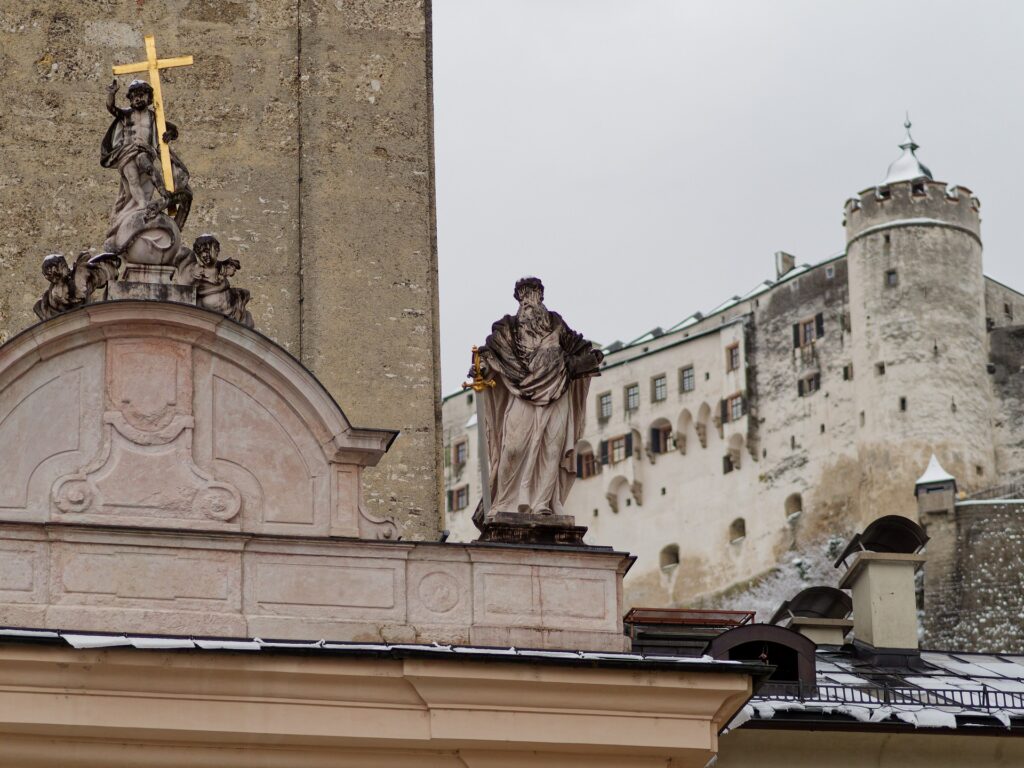 Barocke Figuren auf der Stiftskirche St. Peter mit Festung im Hintergrund.