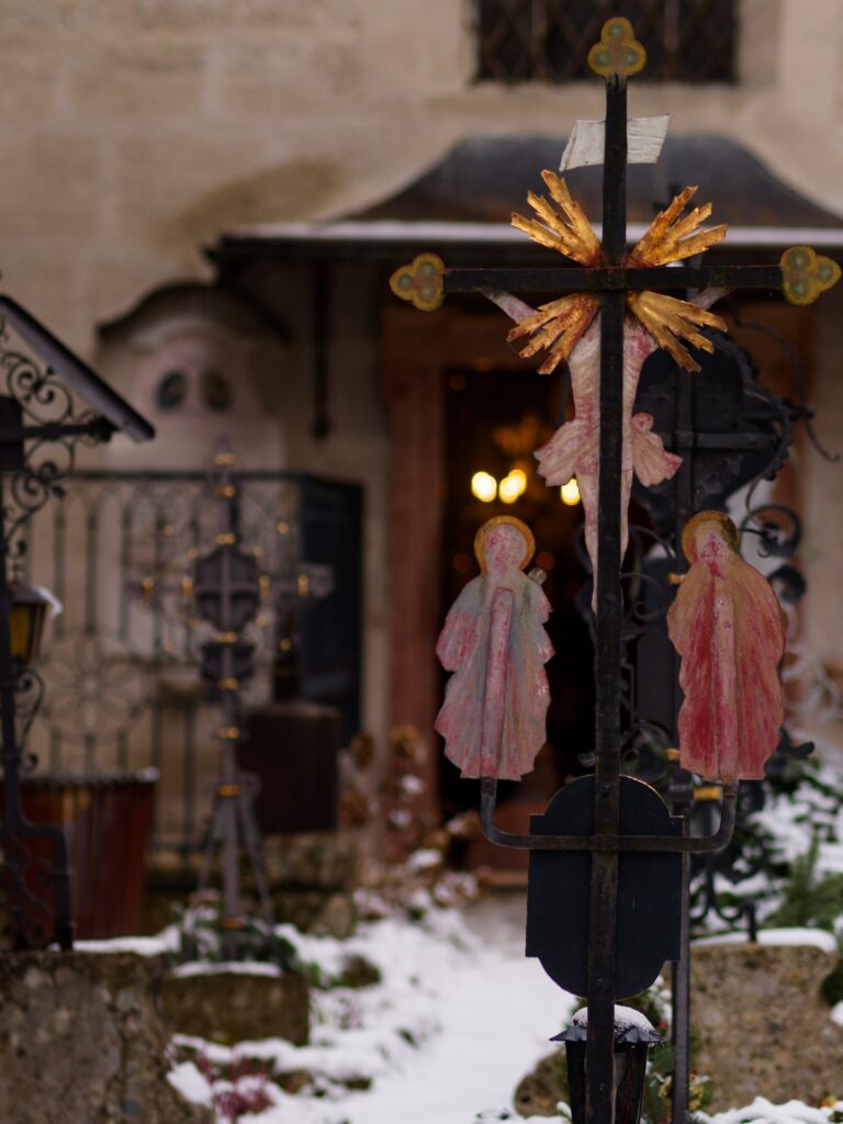 Schmiedeeisernes Grabkreuz mit unscharfem Licht im Hintergrund auf dem Petersfriedhof in Salzburg.